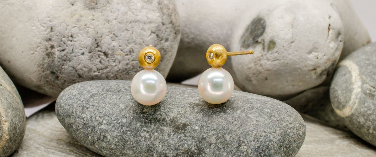 Gold, diamond and pearl stud earrings on rock background