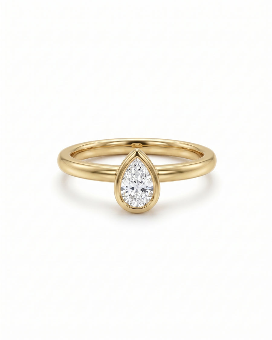 Pear cut diamond engagement ring in a yellow gold bezel setting on a white background.