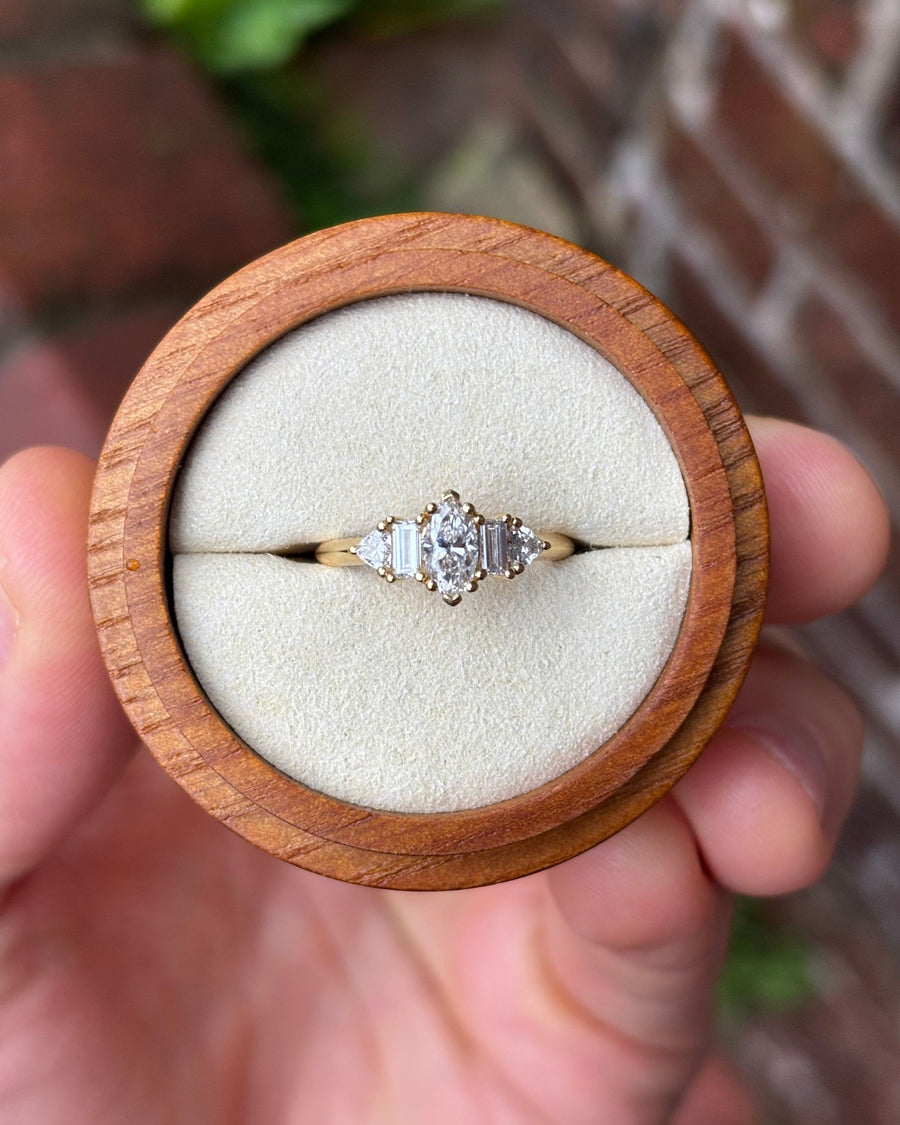 Gold engagement ring featuring a marquise cut center stone with baguette and triangle side diamonds.