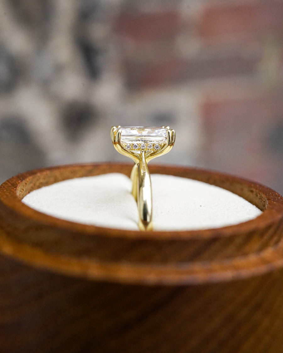 Radiant cut diamond engagement ring in yellow gold with a hidden halo setting in a wooden box.