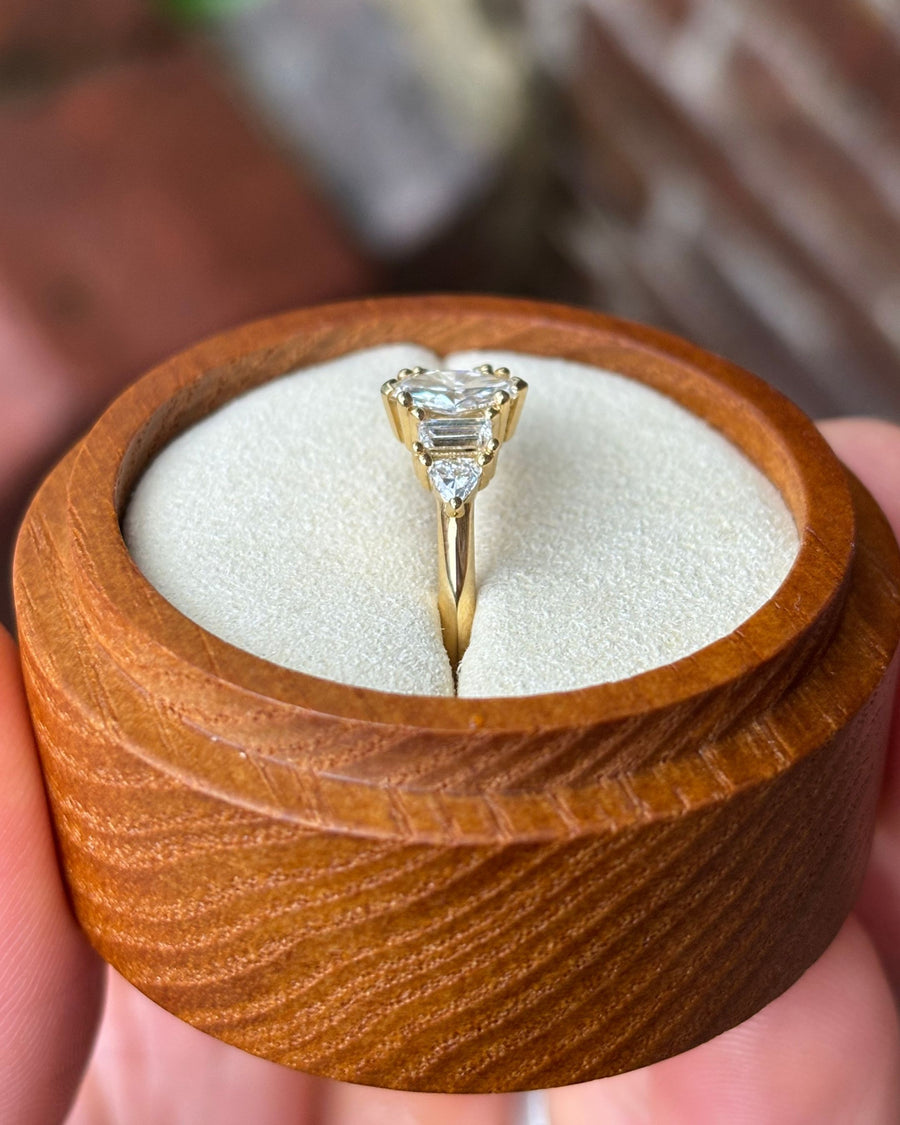 Gold engagement ring with a marquise center stone and baguette and trillion side stones in a wooden box.