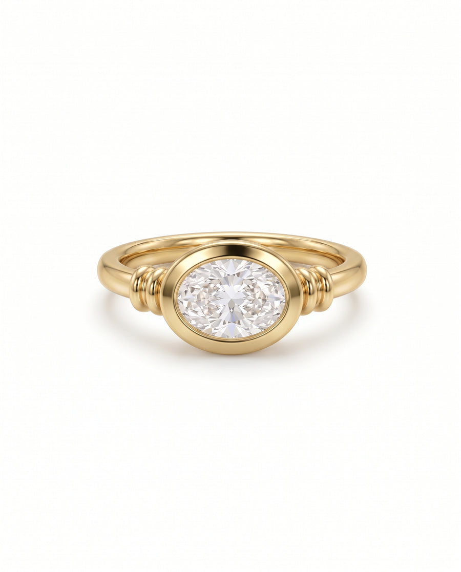 Gold engagement ring featuring an east-west oval diamond in a bezel setting with ribbed band details.