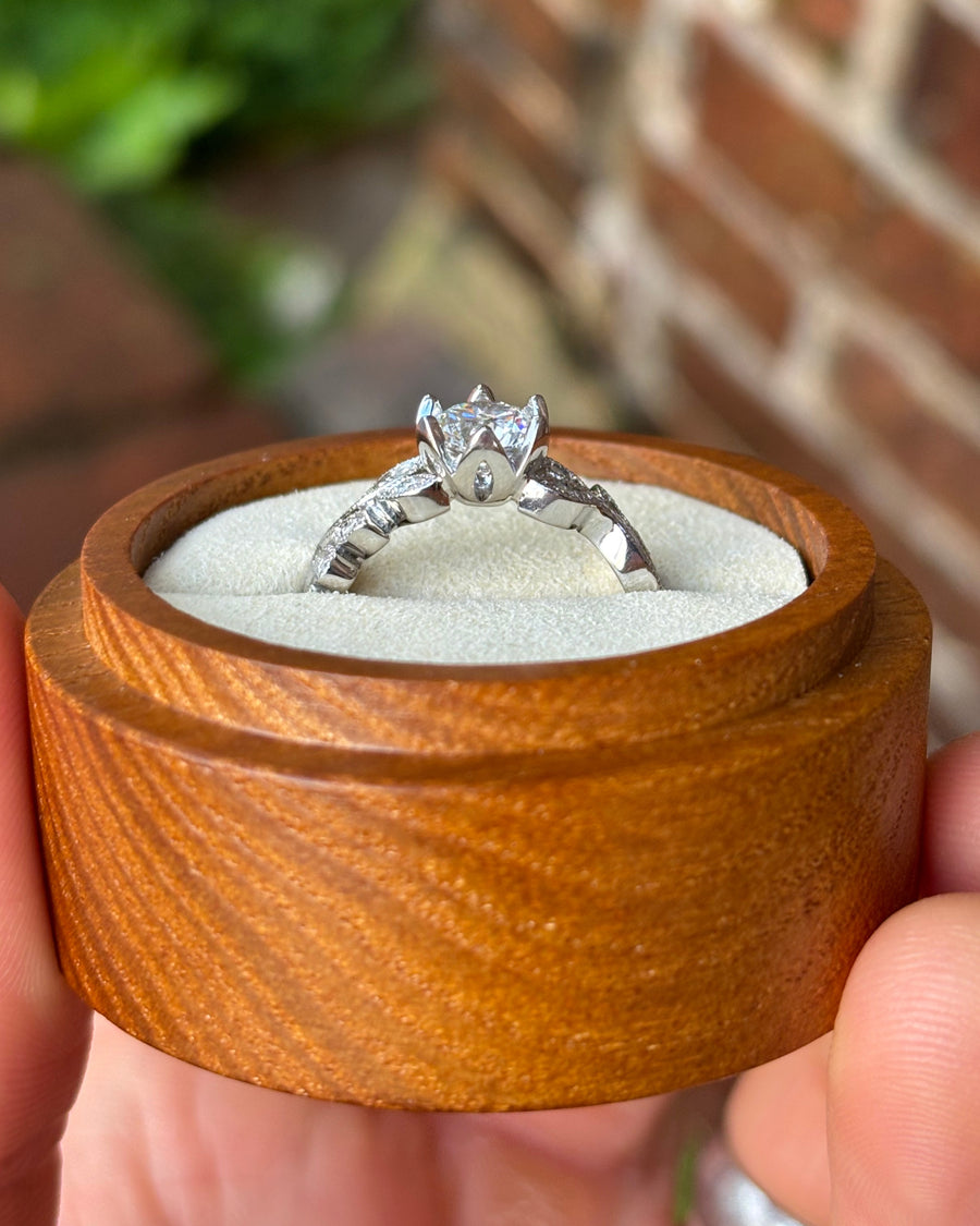 Vintage silver diamond engagement ring with a floral setting in a round wooden box.