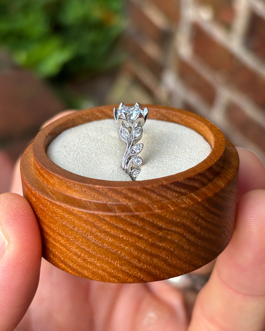 Vintage silver engagement ring with a diamond center stone and leaf-inspired band in a wooden box.