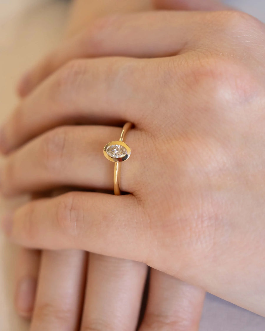 Gold engagement ring with an oval cut natural diamond in a bezel setting.
