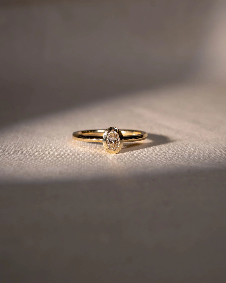 Gold engagement ring with an oval cut natural diamond in a bezel setting.