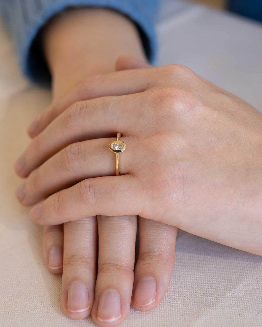 Gold bezel engagement ring with an oval cut diamond on a hand.