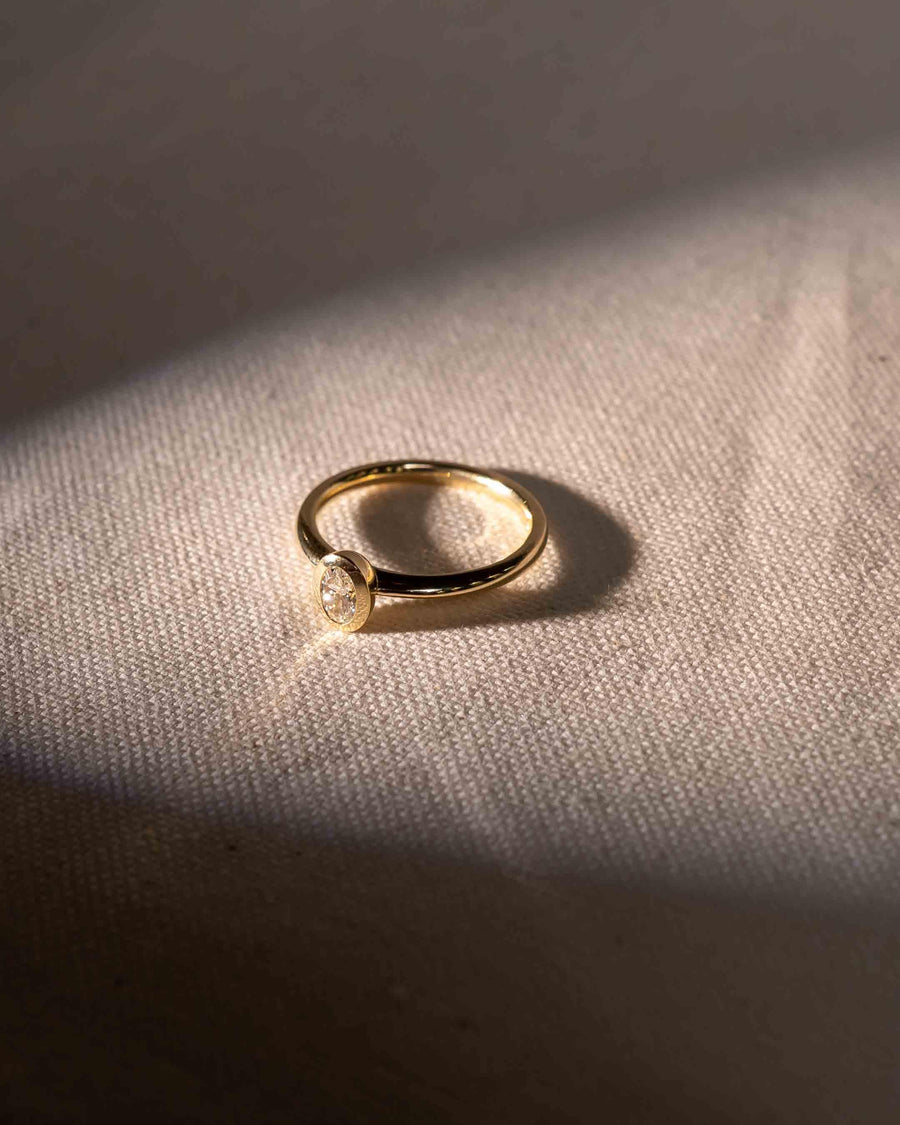 Gold ring with an oval cut natural diamond in a bezel setting.