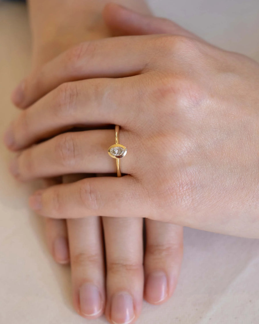 Gold bezel engagement ring with an oval cut natural diamond on a hand.