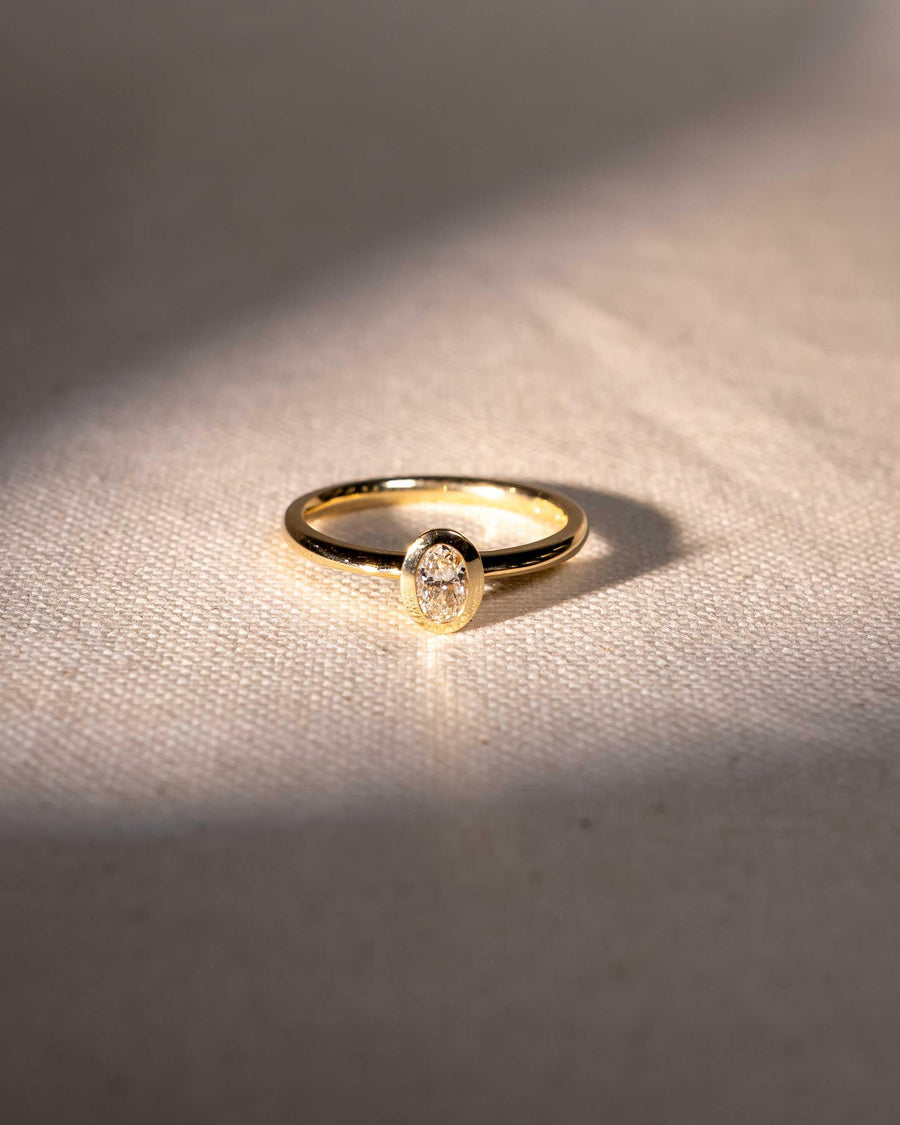 Gold ring with an oval-cut natural diamond in a bezel setting.