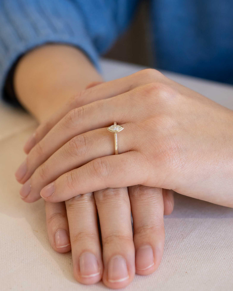 Yellow gold ring with a marquise cut natural diamond in a bezel setting on a hand.