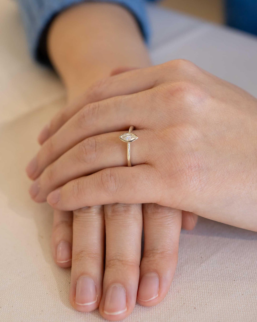 Gold ring with a marquise cut diamond in a bezel setting on a hand.