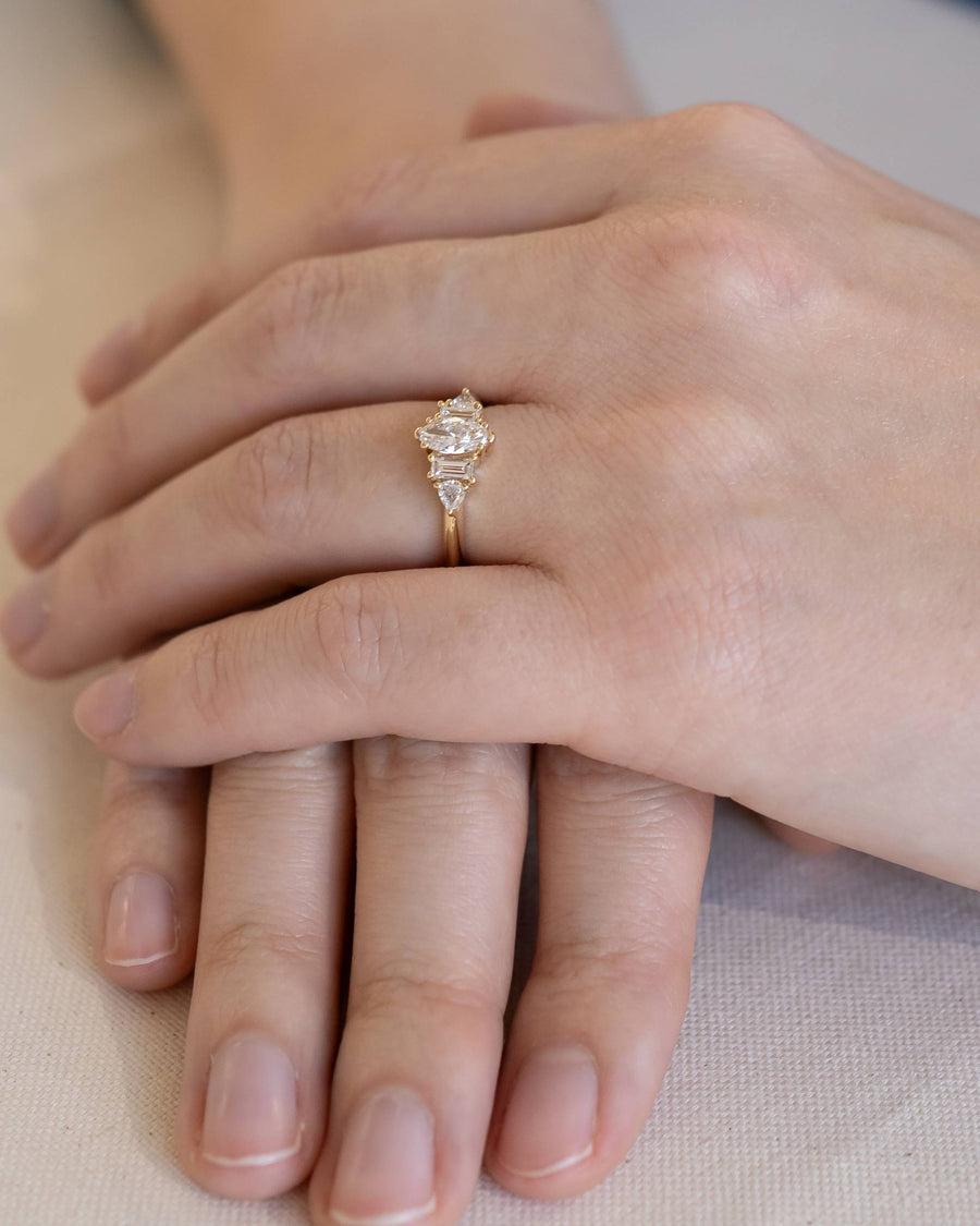 Gold marquise cut diamond engagement ring with claw side stones on a hand.