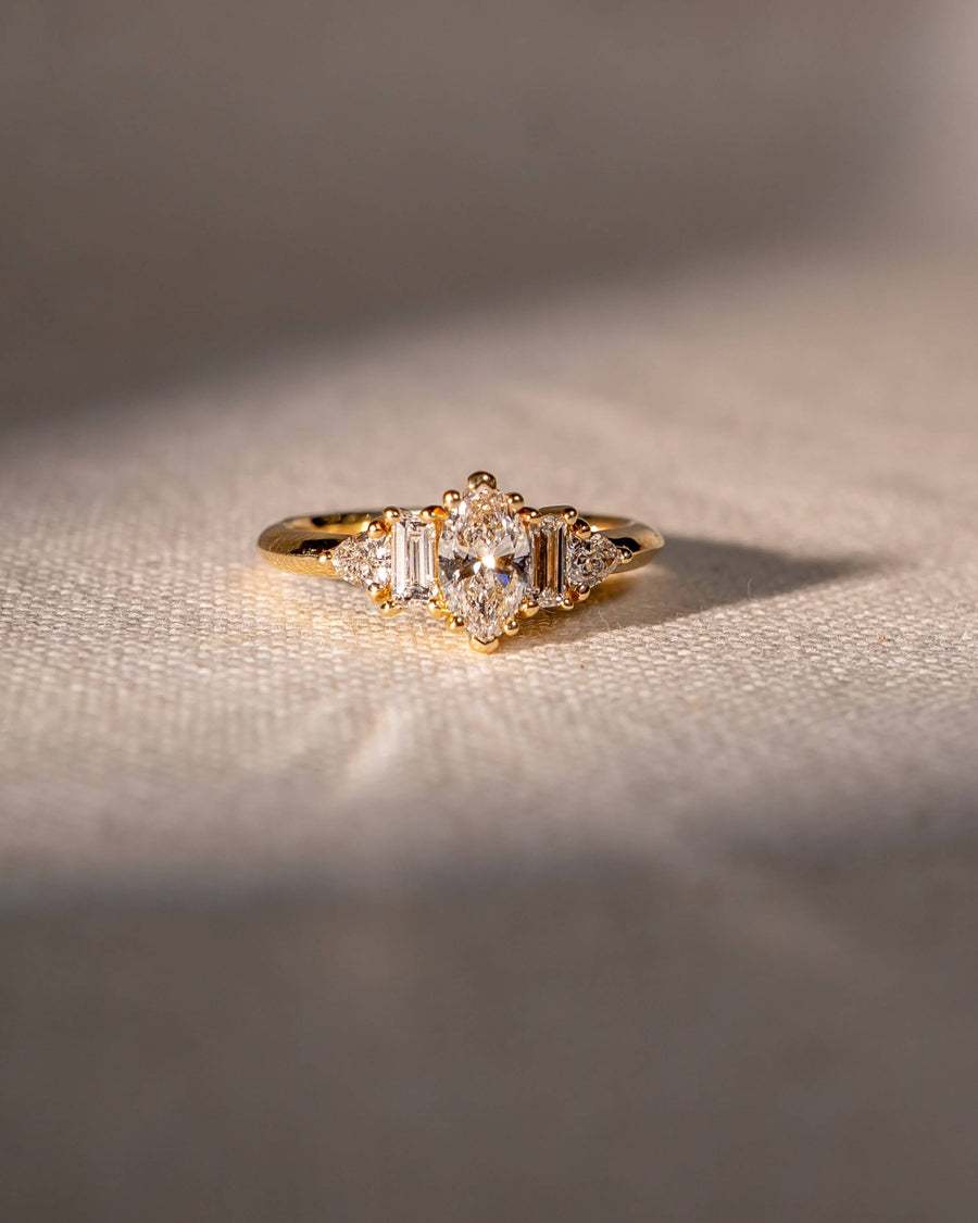 Gold engagement ring with a marquise cut diamond and claw side stones.