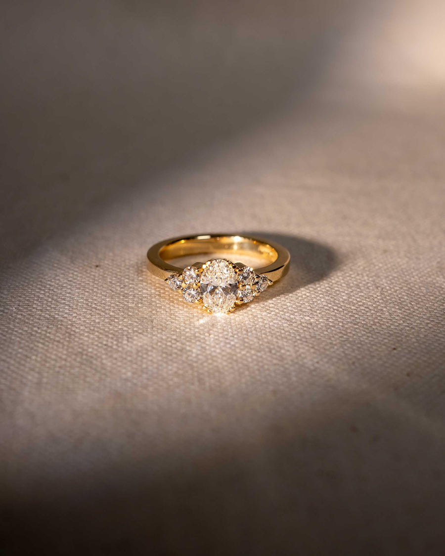 Gold ring with oval diamond and cluster of diamonds on textured fabric background, luxury handmade jewellery