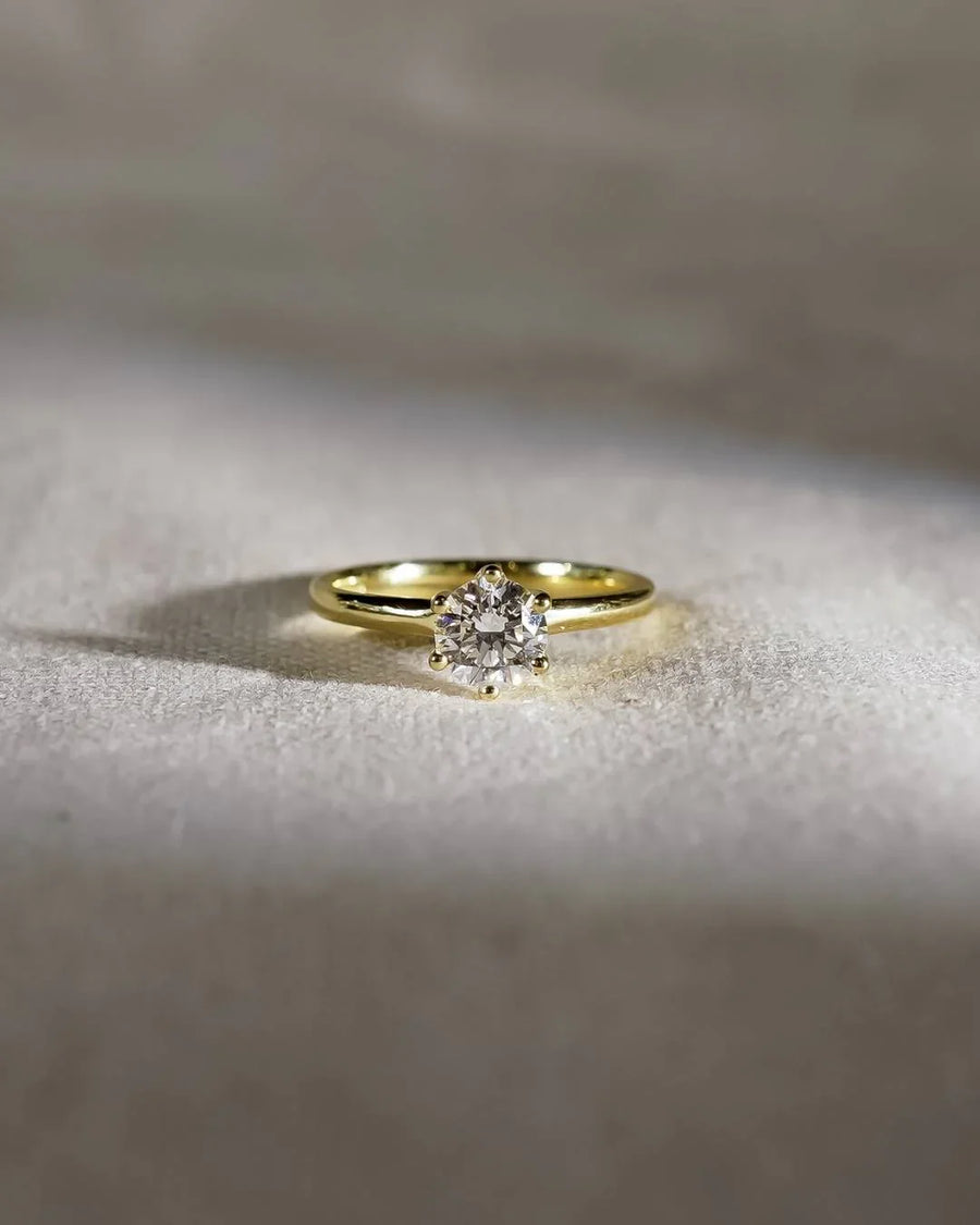 Round solitaire diamond engagement ring with a yellow gold band on light fabric background