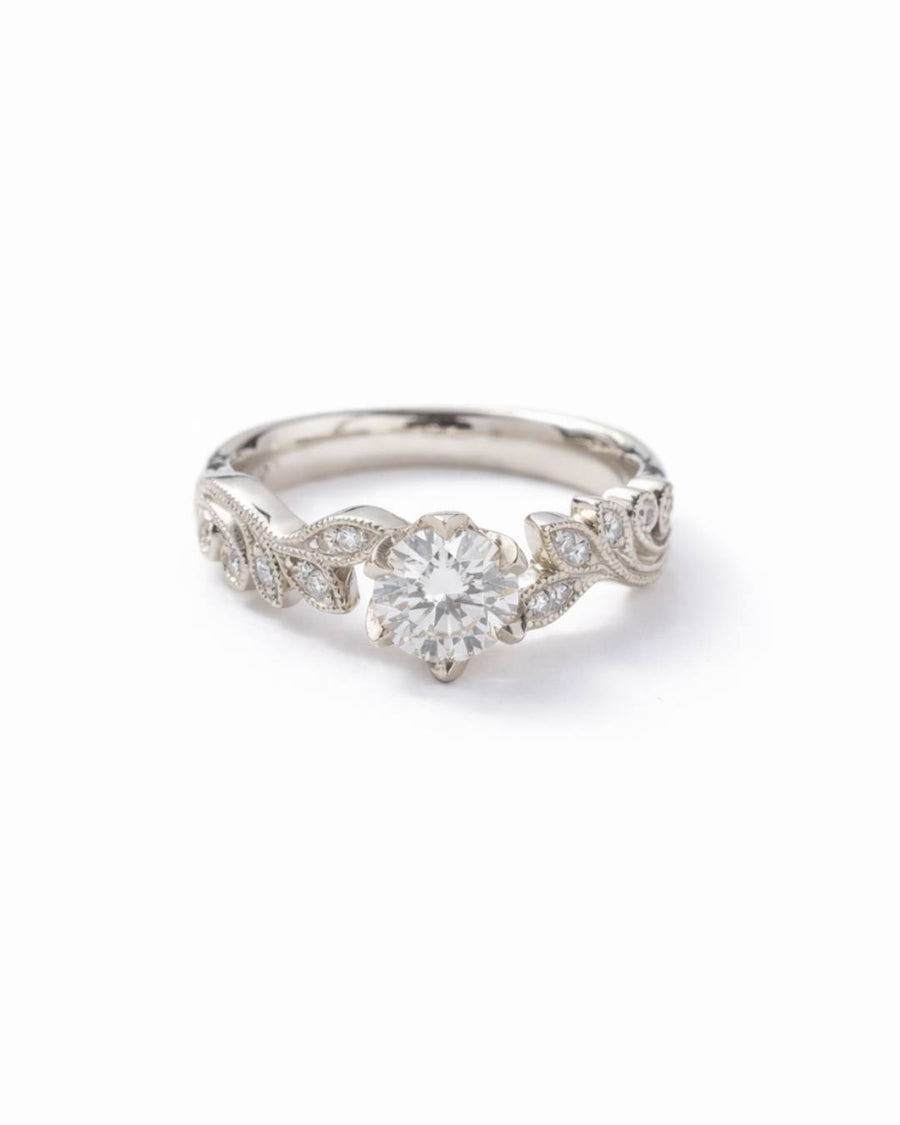 Platinum engagement ring with a round diamond center and beaded leaf design.