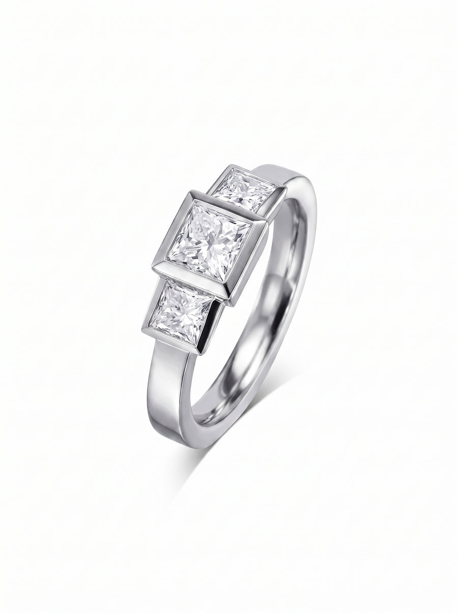 Trilogy engagement ring featuring three princess cut diamonds in a silver-toned metal bezel setting.