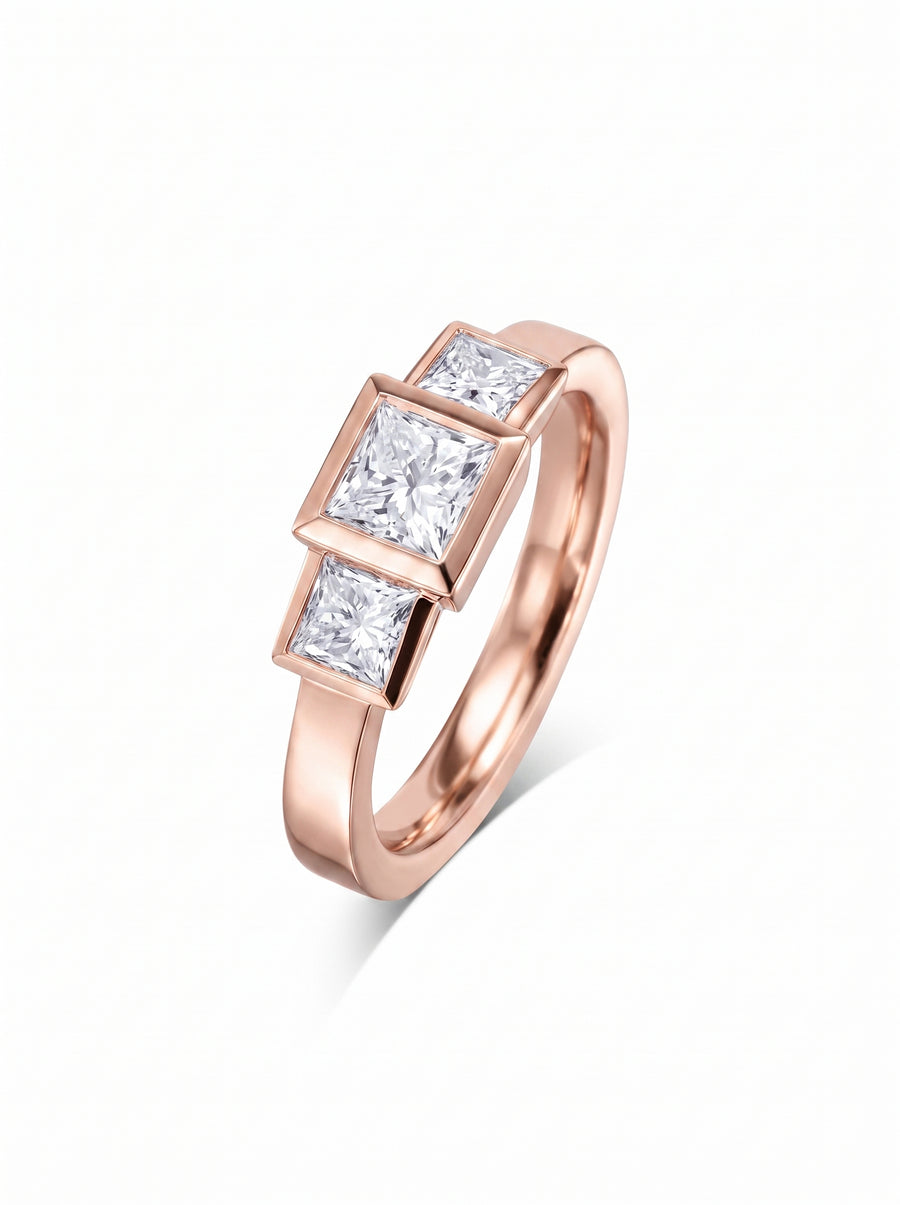 Rose gold trilogy engagement ring featuring three bezel-set princess cut diamonds in an art deco style.