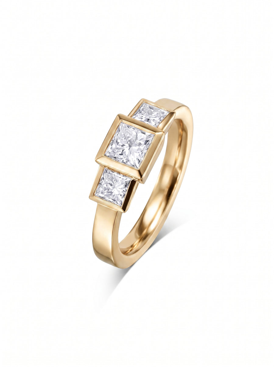 Gold trilogy engagement ring featuring three bezel-set princess cut diamonds in a polished yellow gold band.