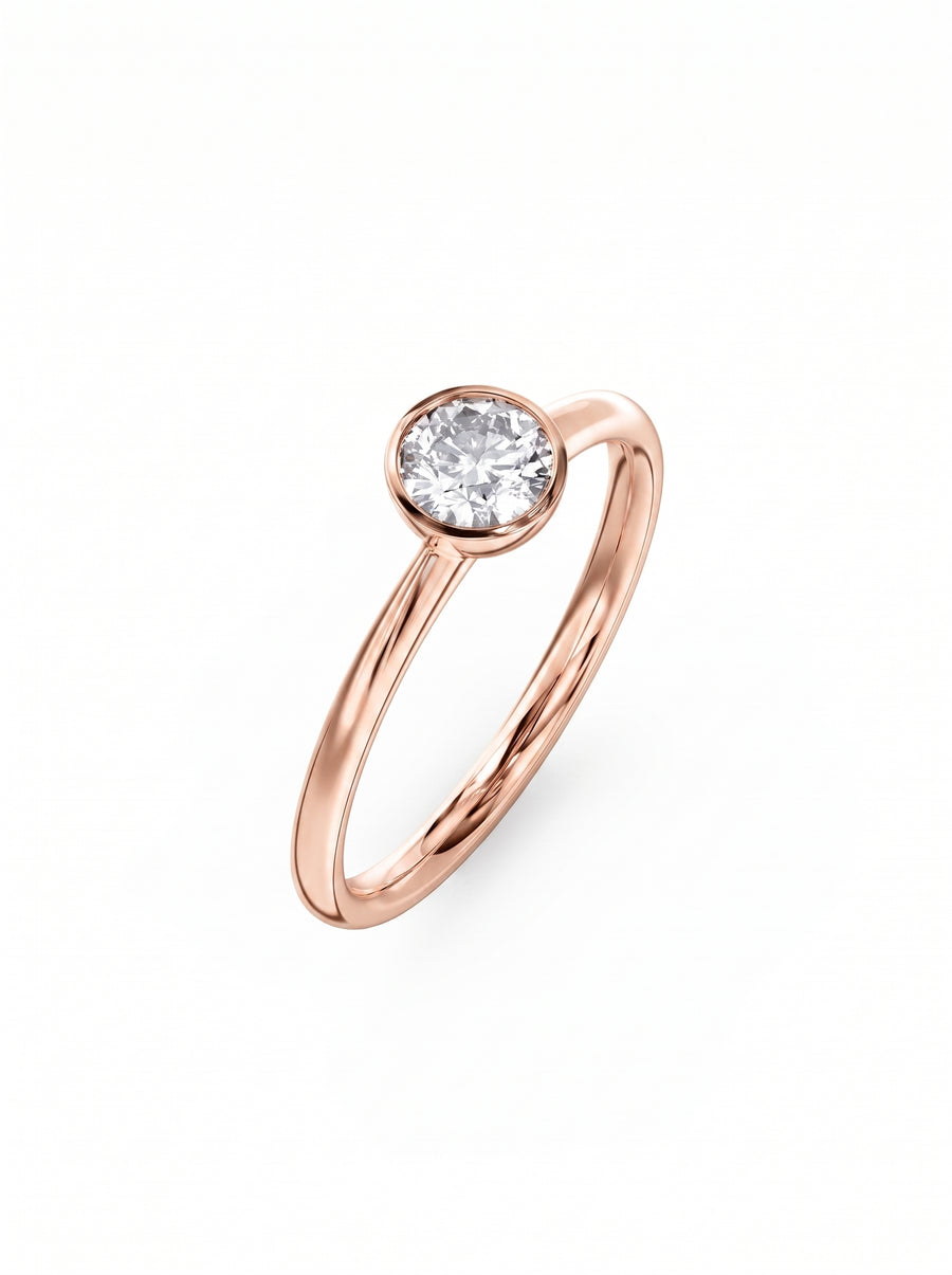 Round cut diamond engagement ring in a rose gold bezel setting on a white background.