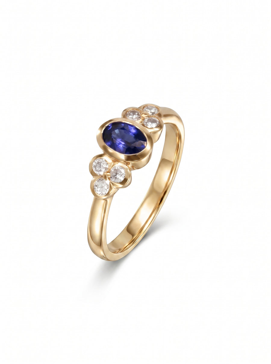 Gold engagement ring featuring an oval blue sapphire flanked by clusters of small round diamonds.