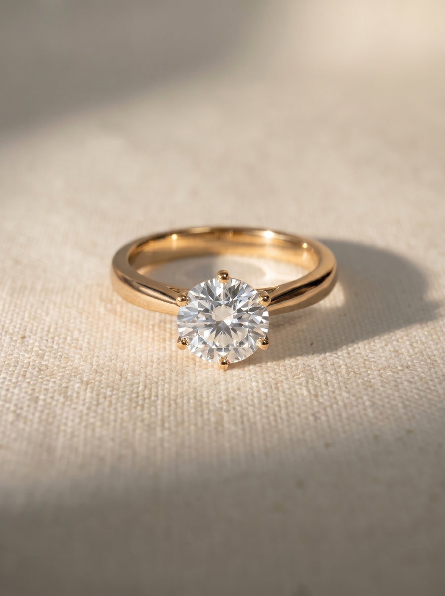 Round brilliant cut diamond engagement ring with a six-claw setting on a polished yellow gold band.
