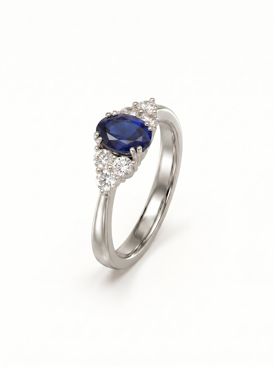 Oval blue sapphire and round diamond trefoil engagement ring set in polished white gold.