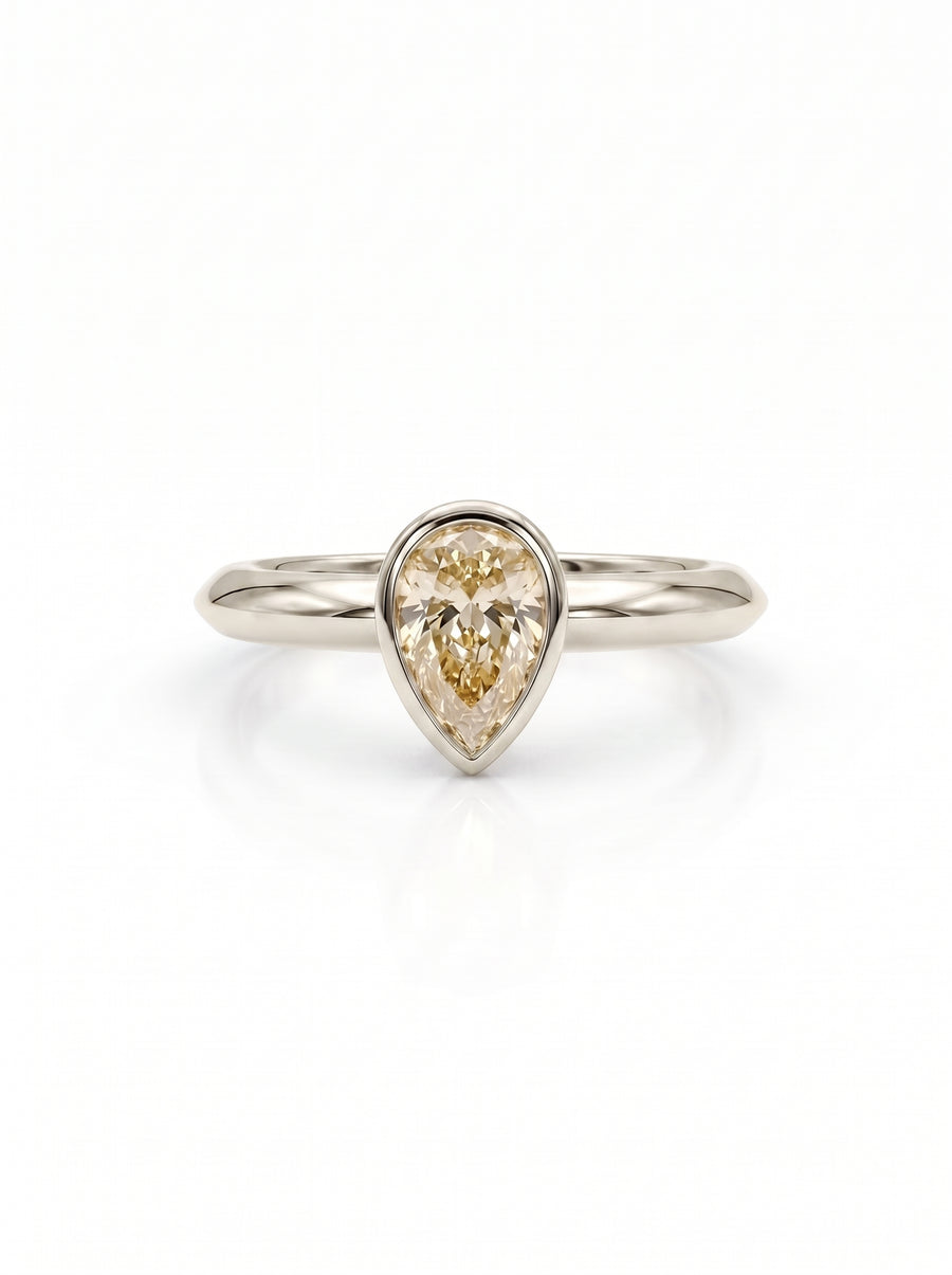 Pear cut champagne diamond solitaire ring in a gold bezel setting on a polished gold band.