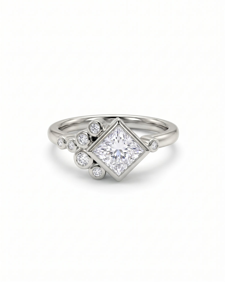 Princess cut diamond engagement ring in silver metal with a cluster of round accent stones.