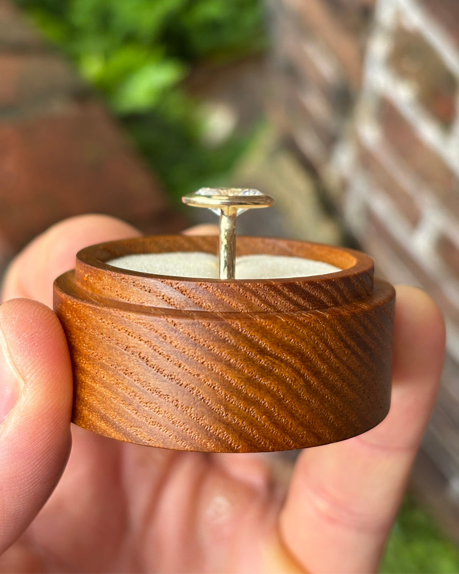 Oval cut lab-grown diamond engagement ring in a gold bezel setting on a wooden ring box.