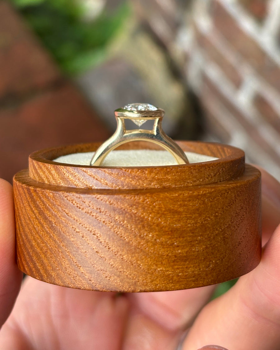 Oval cut lab-grown diamond engagement ring in a gold bezel cathedral setting inside a wooden box.