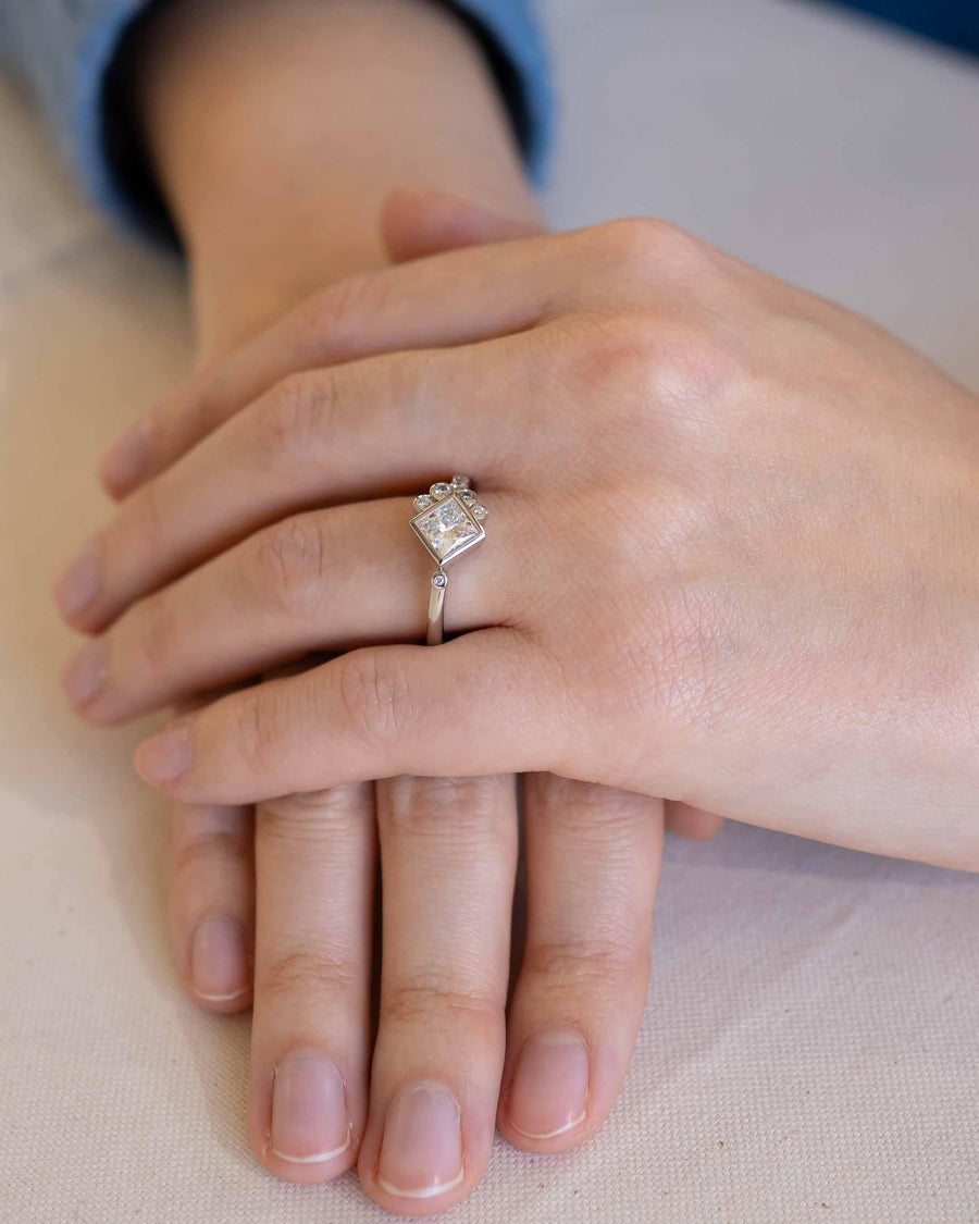 Platinum ring with an emerald cut lab-grown diamond and side stones on a hand.
