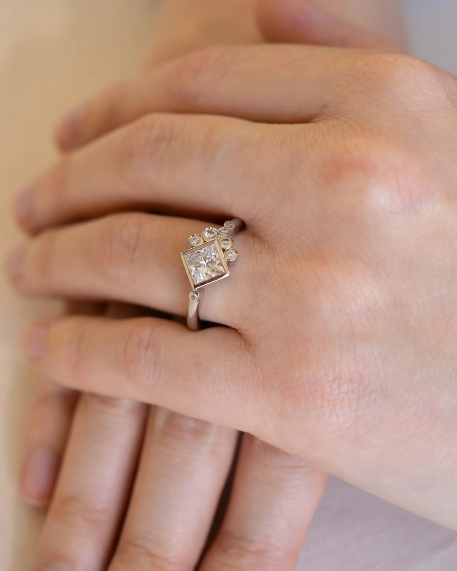 Platinum ring with an emerald cut lab-grown diamond and round accent diamonds on a hand.