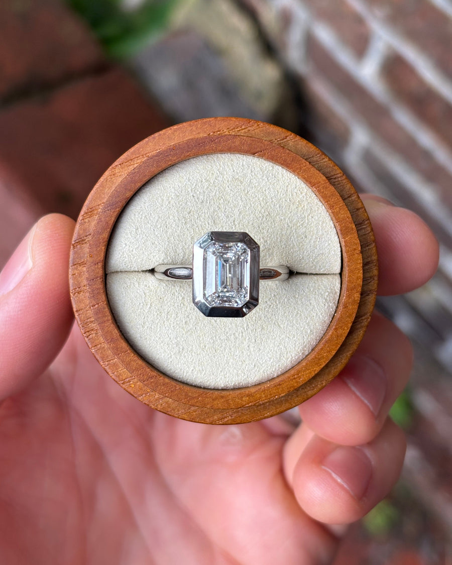 Emerald cut lab-grown diamond engagement ring in a platinum bezel setting held in a wooden box.