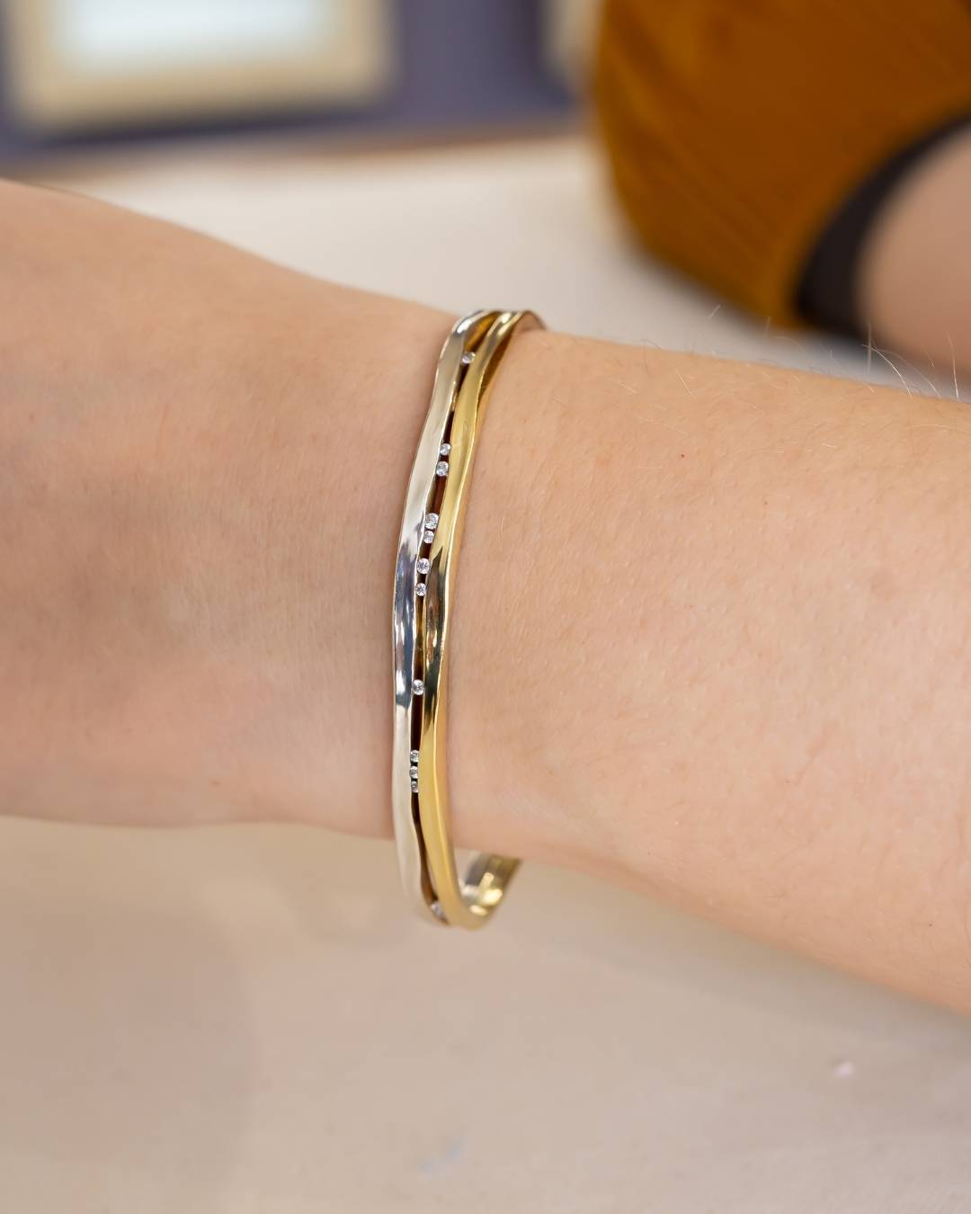 Hand wearing an elegant gold and silver bangle with organic textured design