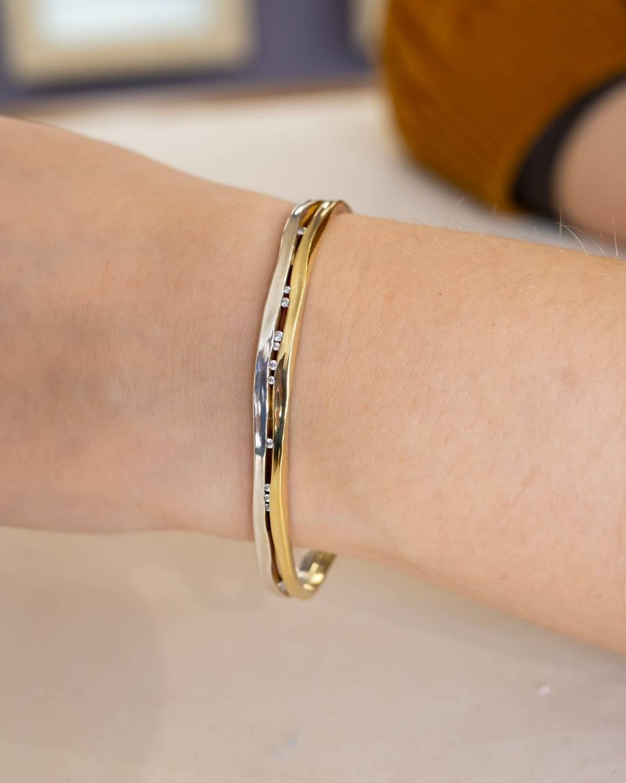 Hand wearing an elegant gold and silver bangle with organic textured design