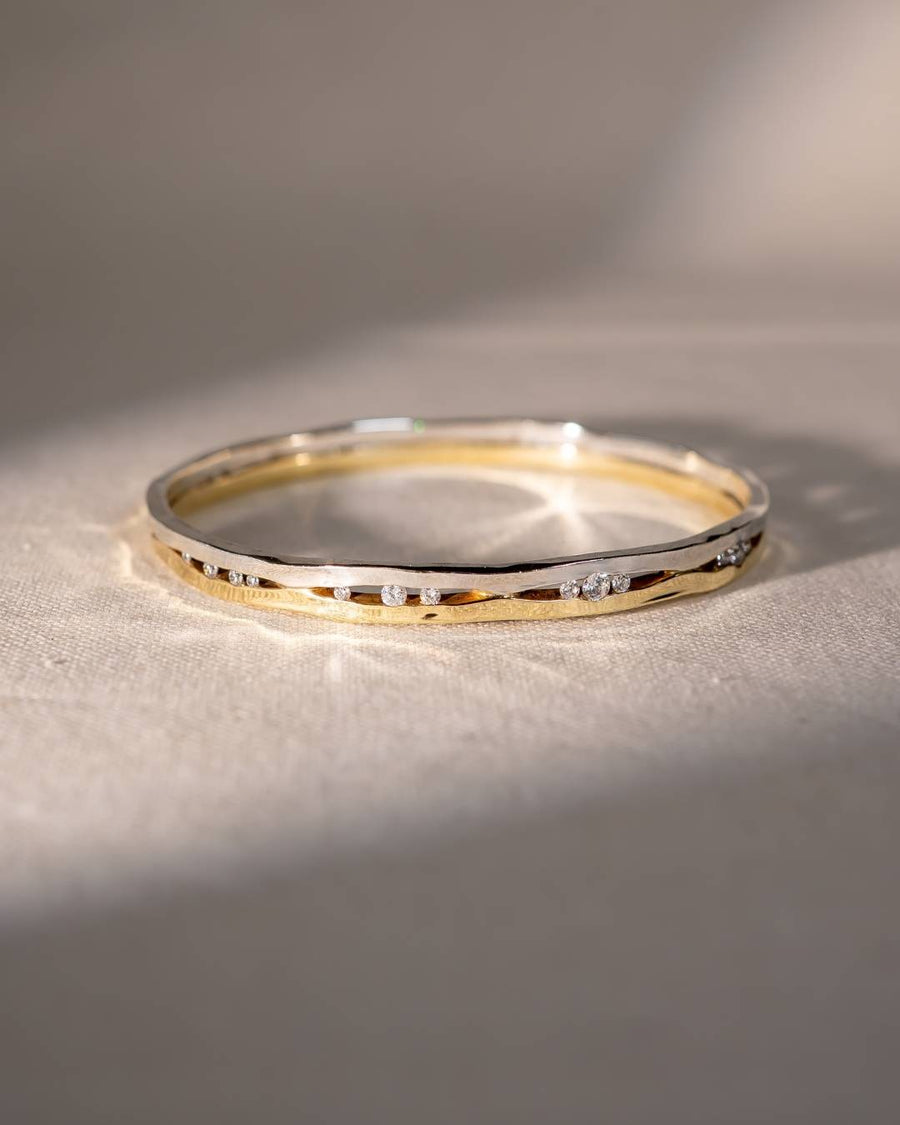 Handmade gold and silver bangle with organic shape and scattered diamonds on fabric