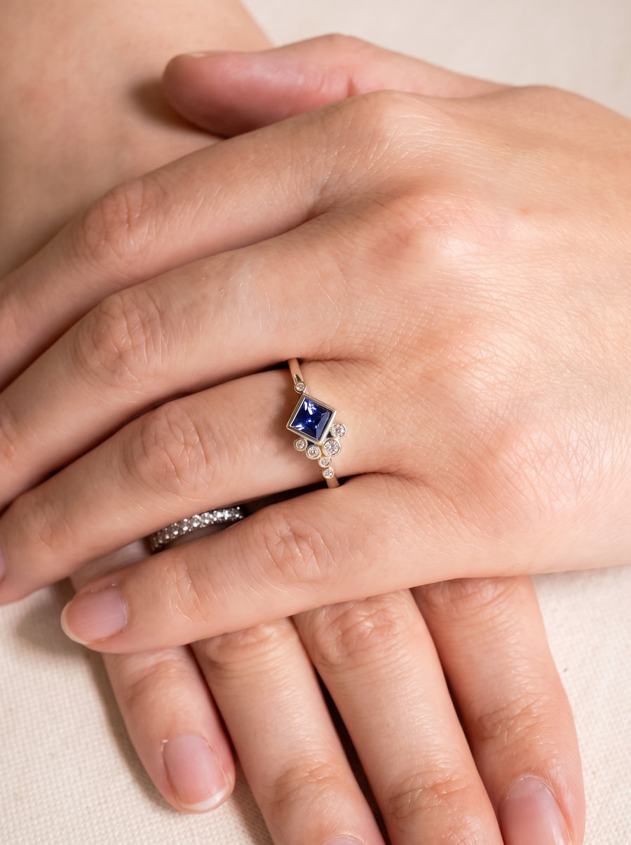 Gold engagement ring featuring a square blue sapphire and small round diamonds on a thin band.