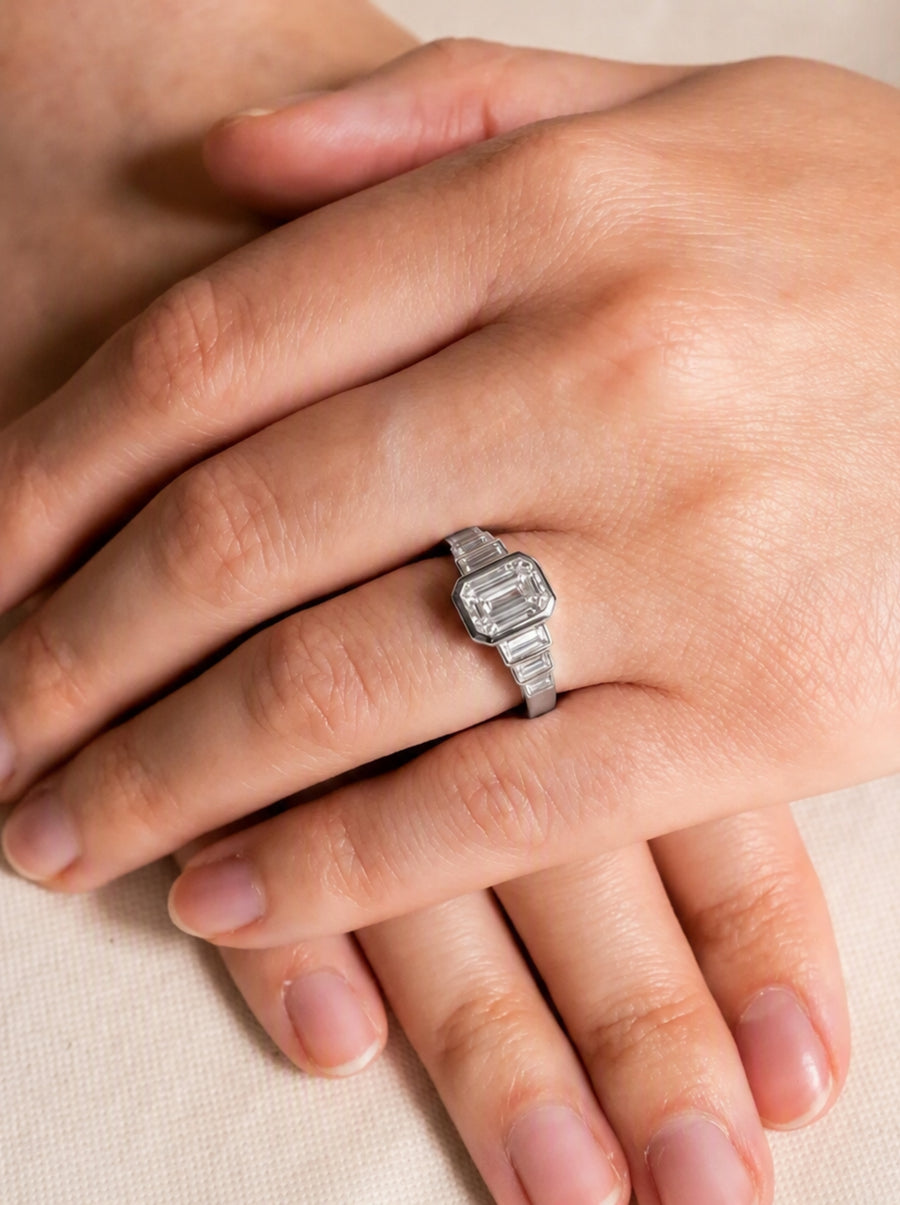 Art deco platinum engagement ring featuring a central emerald cut diamond flanked by three baguette diamonds on each side.
