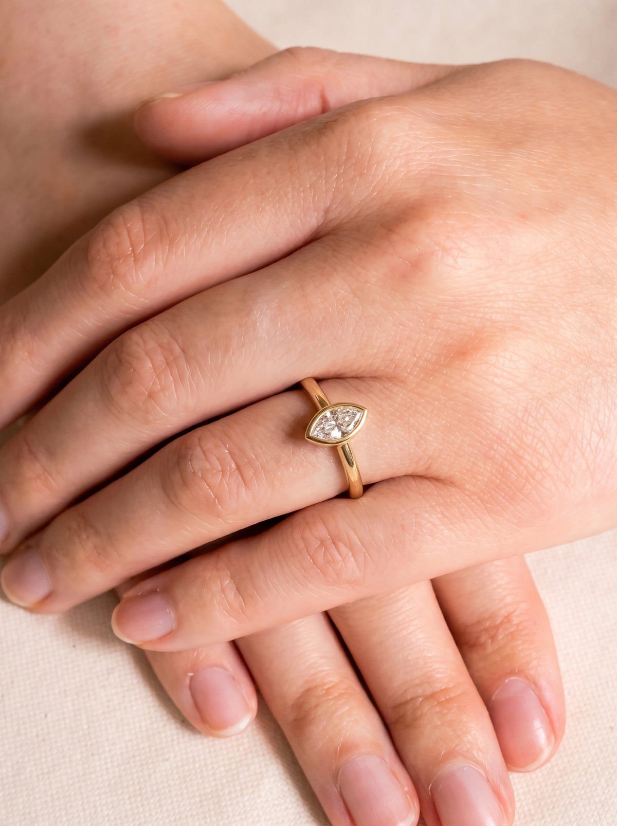 Gold bezel engagement ring featuring a marquise cut diamond on a person's finger.