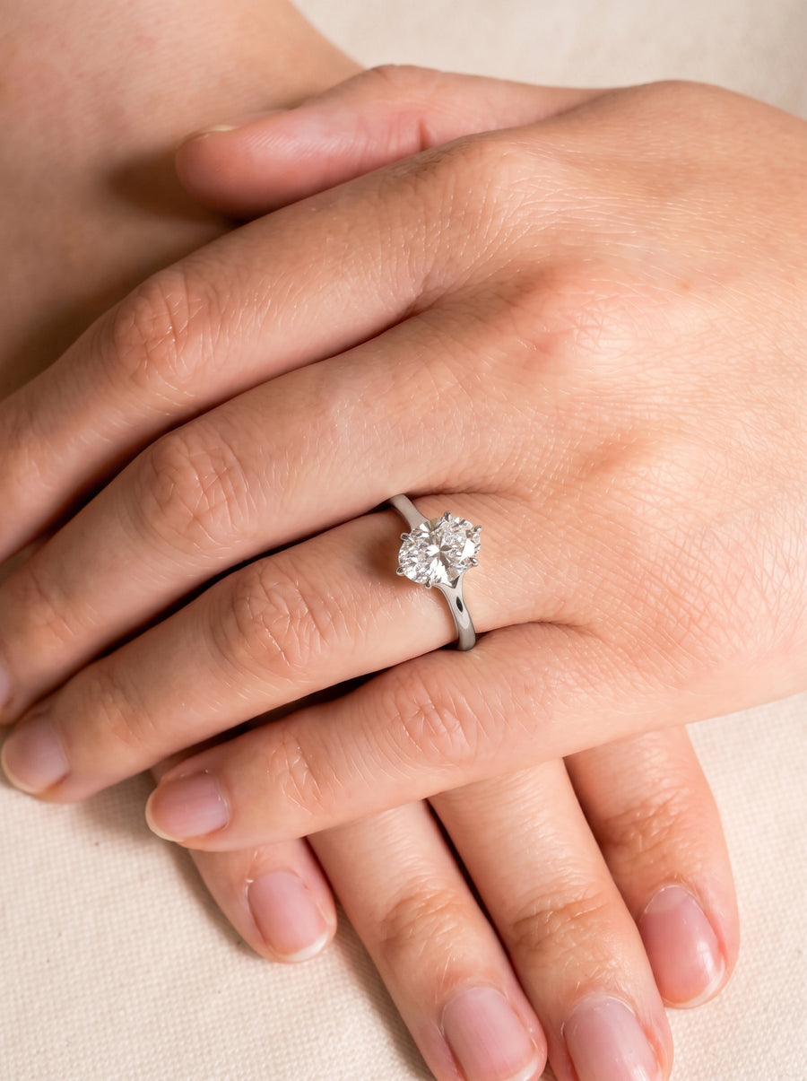 Oval cut diamond engagement ring with a tulip claw setting on a silver band worn on a finger.
