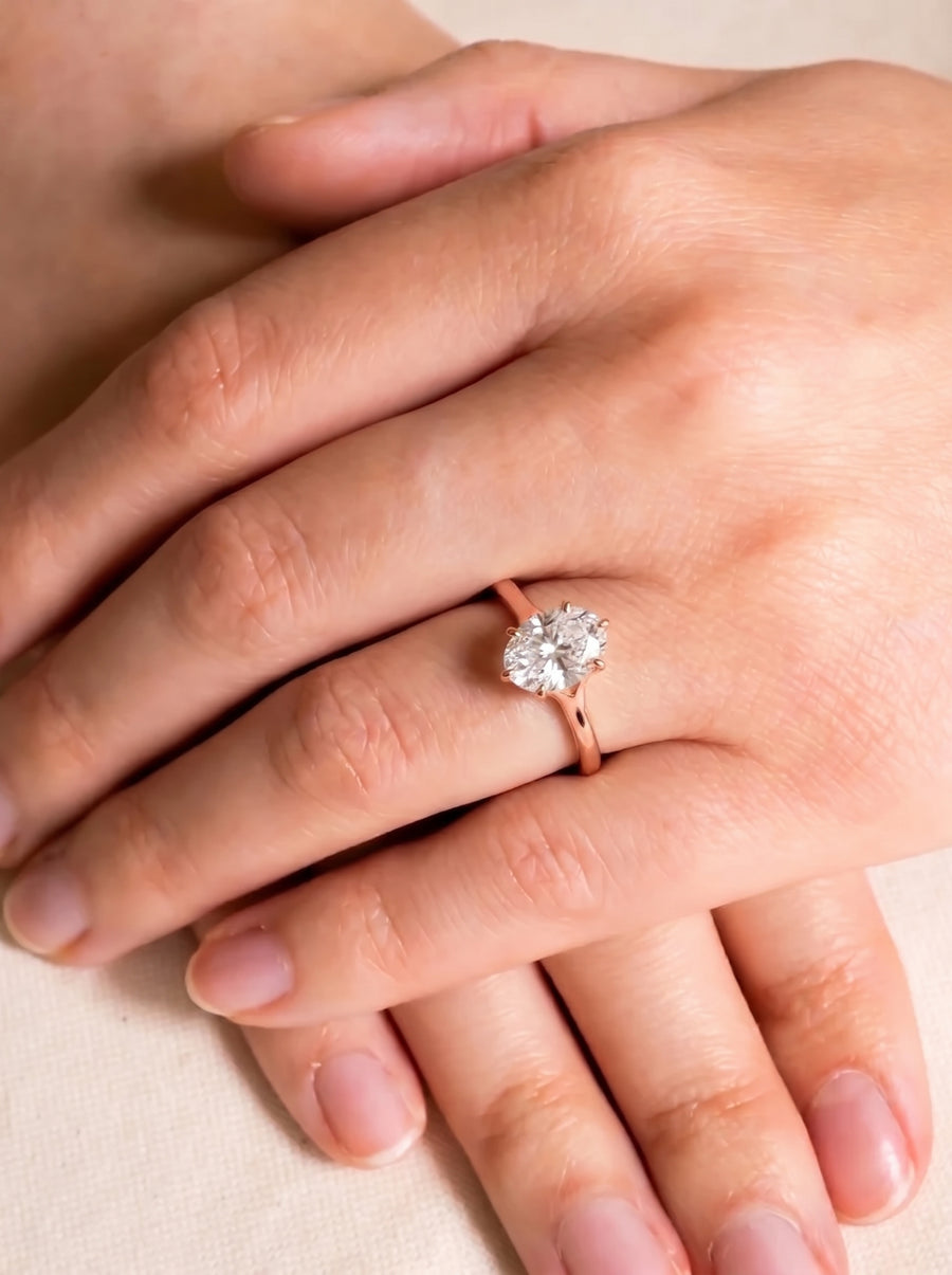 Oval cut diamond engagement ring with a tulip claw setting on a rose gold band worn on a finger.