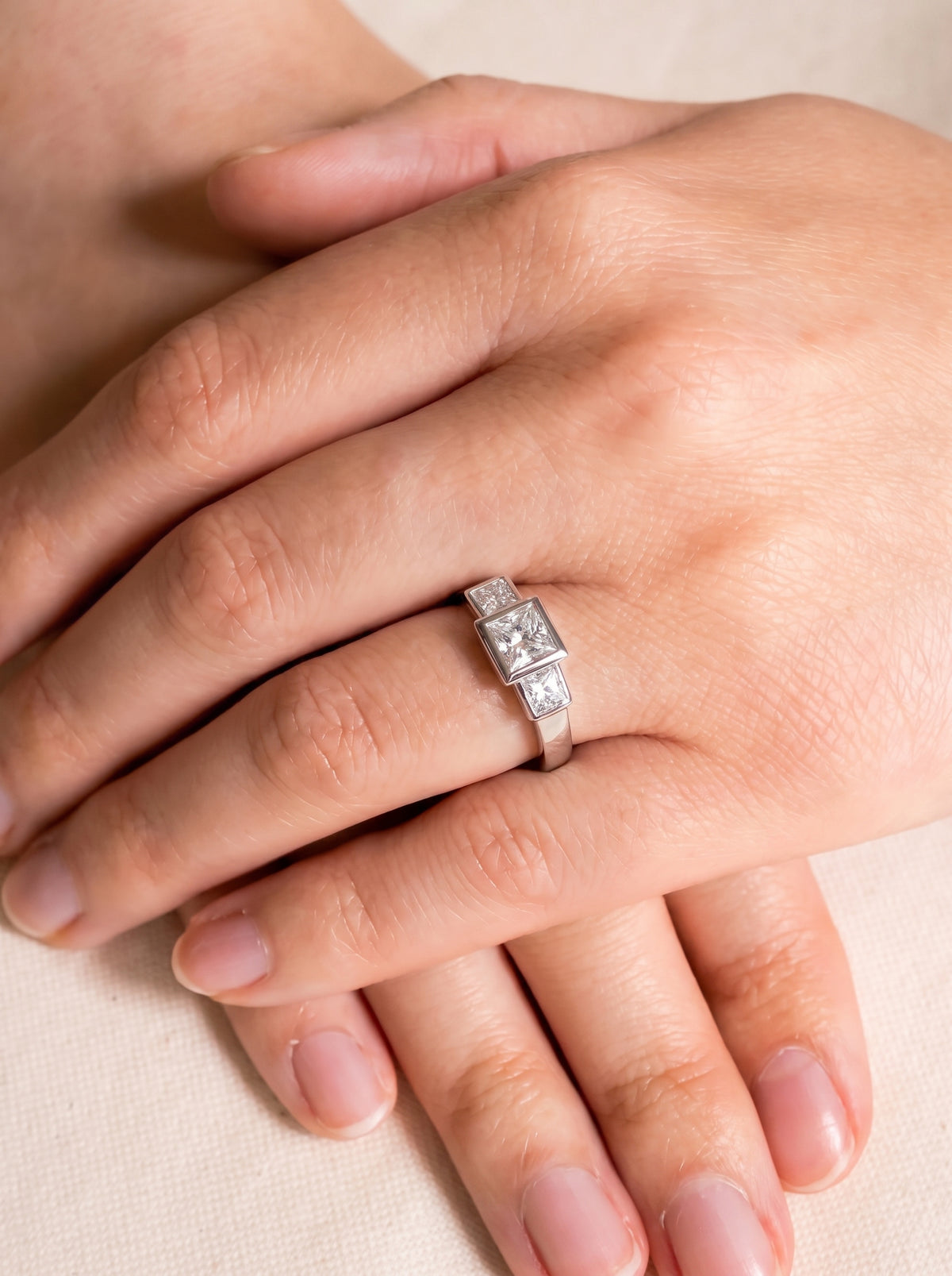 Three-stone engagement ring with princess cut diamonds set in a polished silver-tone band on a finger.