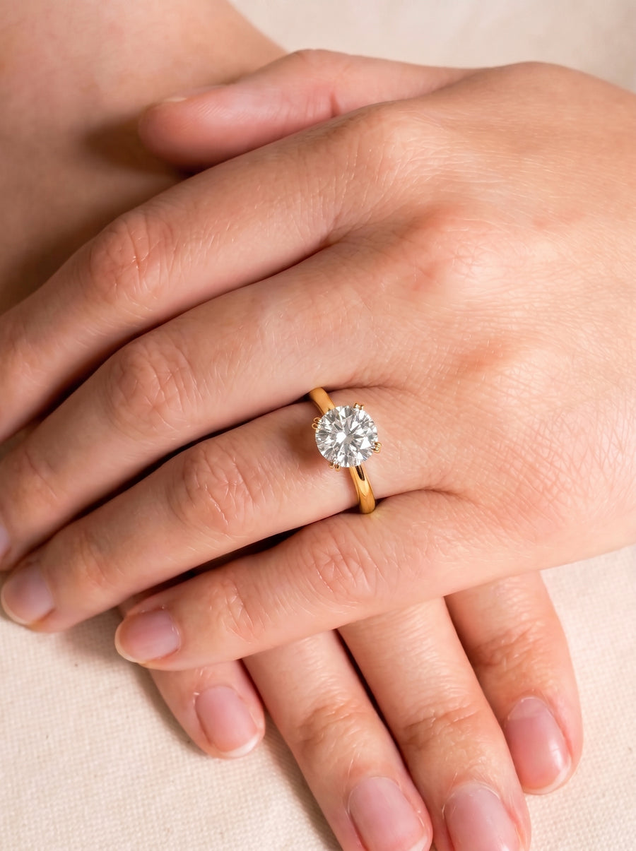 Round cut diamond engagement ring with a hidden halo on a gold band worn on a finger.