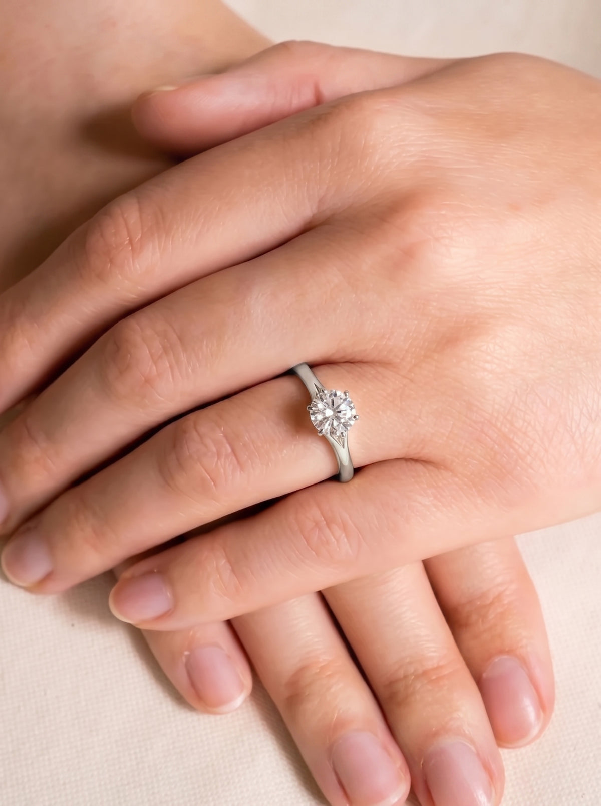 Round cut diamond engagement ring with a silver tulip claw setting worn on a finger.