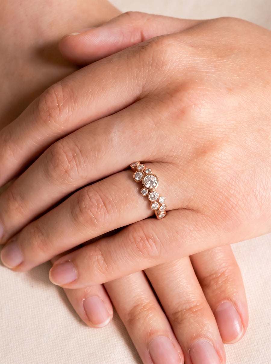 Rose gold ring with bezel-set round diamonds in a cluster bubble design worn on a finger.