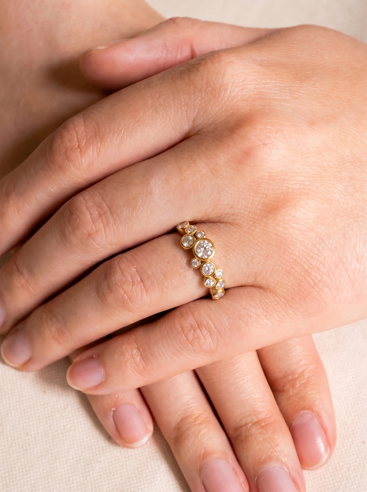Gold engagement ring featuring a cluster of round-cut diamonds in a bubble-inspired bezel setting on a finger.