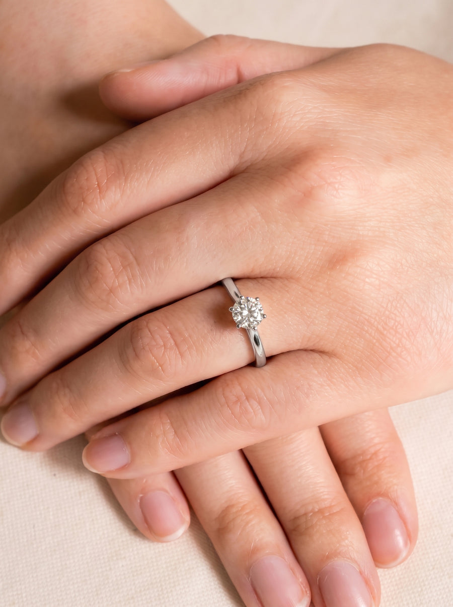 Round diamond solitaire engagement ring with a six-claw setting on a silver band worn on a finger.