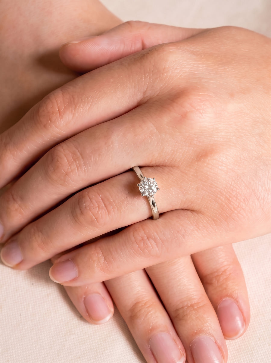 Round diamond solitaire engagement ring with a six-claw setting on a polished silver band worn on a finger.